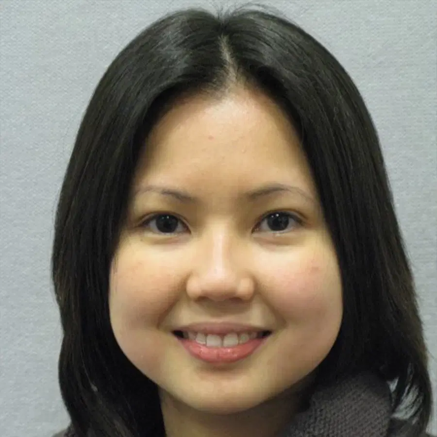 A young woman with straight black hair, fair skin, and dark eyes smiles softly at the camera, set against a plain light grey background.