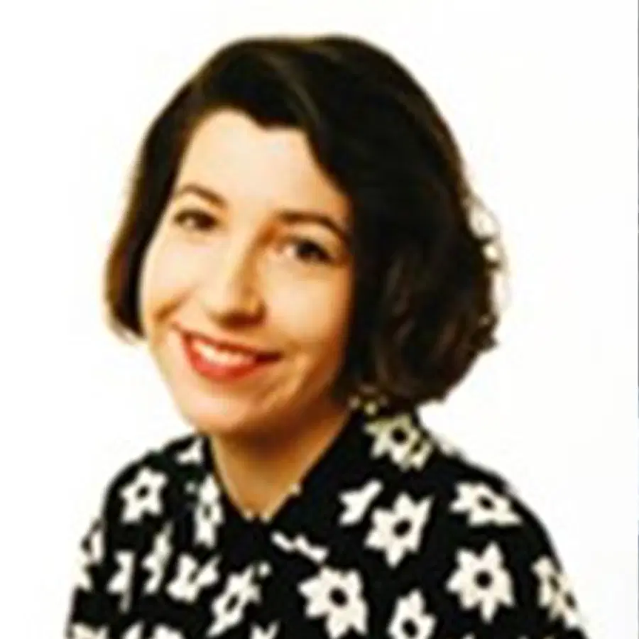 Smiling person with short dark hair wearing a black shirt with white flower patterns, photographed against a plain white background.