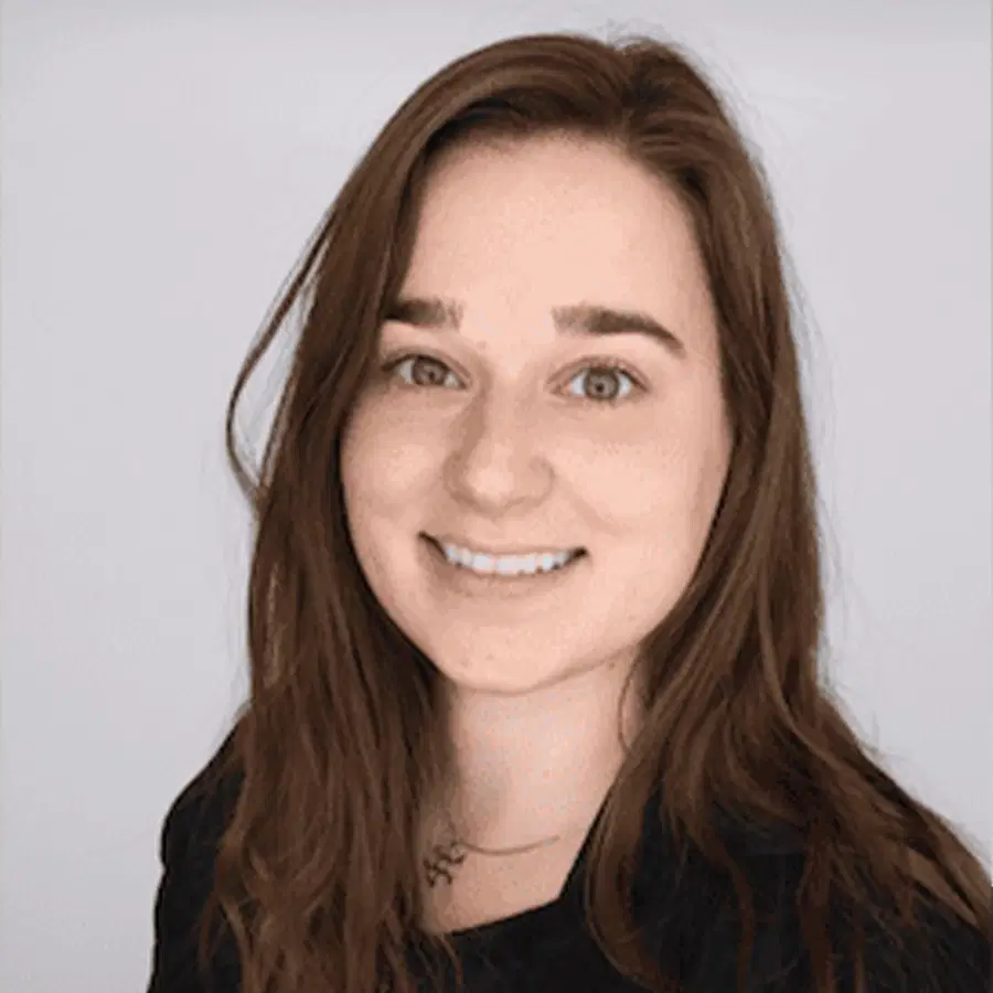 A young woman with long brown hair and a black shirt smiles at the camera, against a plain light background.