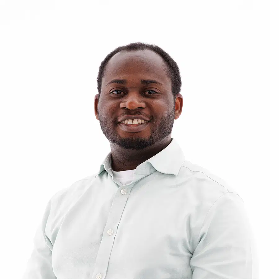 A man with short hair and a beard, wearing a light-coloured button-up shirt, smiling and looking at the camera against a white background.