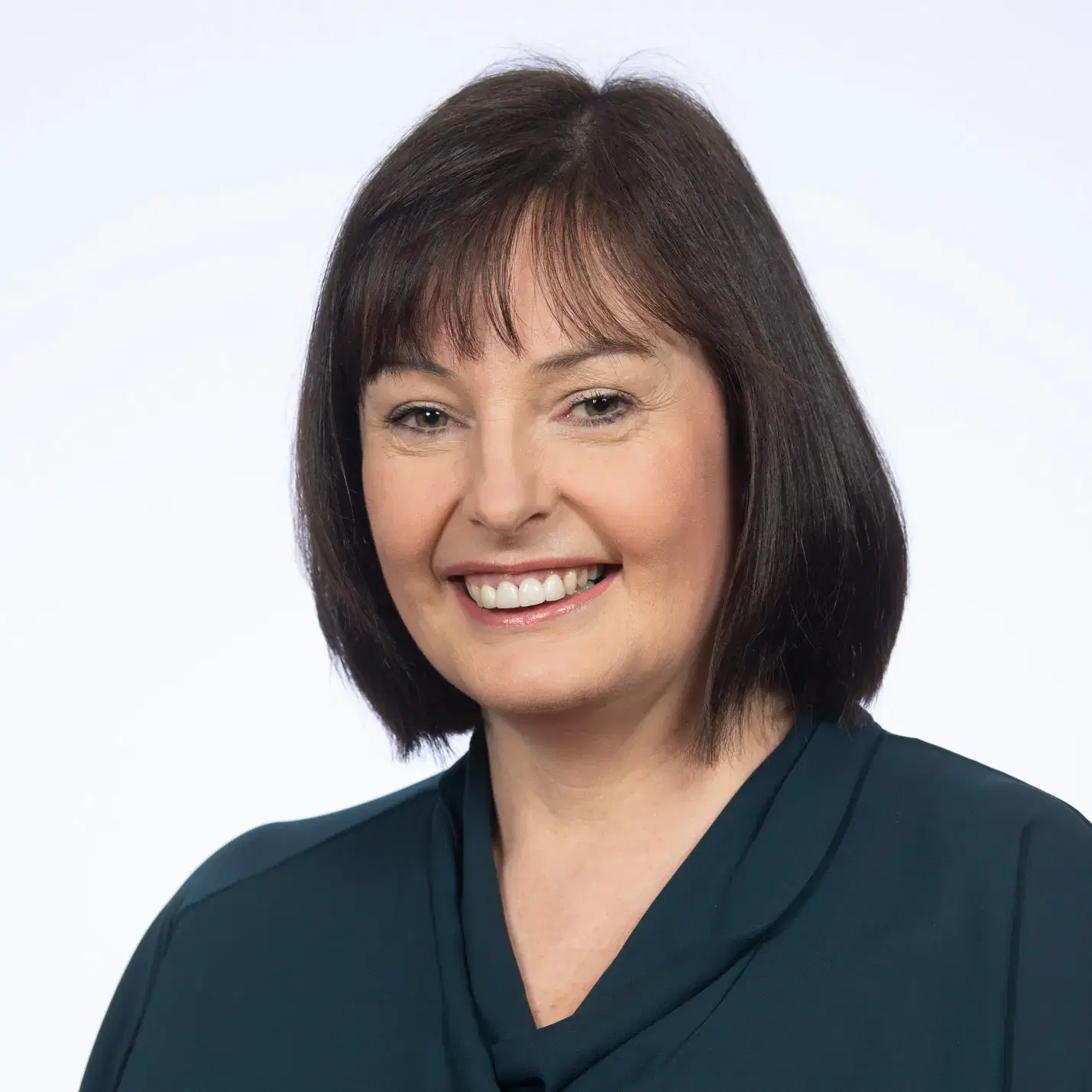 A woman with straight dark hair, wearing a dark green blouse, smiling at the camera against a plain white background.